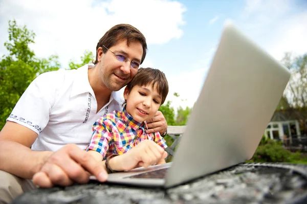 Closeup portrait of happy family: father and his son using laptop outdoor at their backyard sitting on the bench — Stock Photo, Image