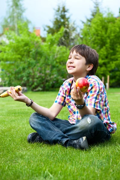 Фото очаровательного молодого мудрого мальчика, сидящего на траве на заднем дворе — стоковое фото