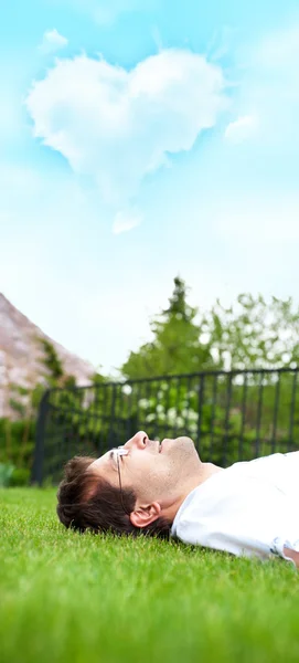 Крупный план портрета молодого красавца в белой рубашке, лежащего на лужайке и мечтающего о любви, глядя на небо — стоковое фото