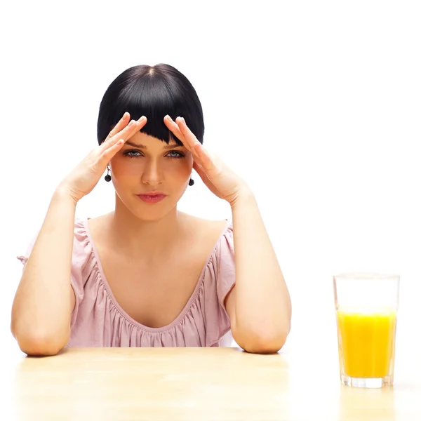 オレンジ ジュースのグラスと彼女のキッチンで座っていた若い女性の肖像画。健康的な食事のコンセプトです。朝食のオレンジ ジュースだけ — ストック写真
