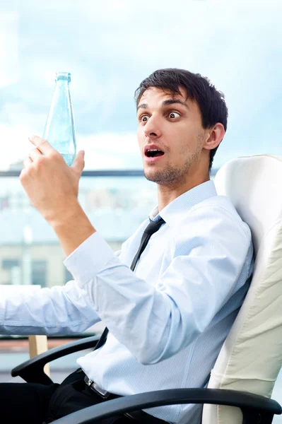 Молодой бизнесмен пьет воду сидя на кресле в своем современном офисе — стоковое фото