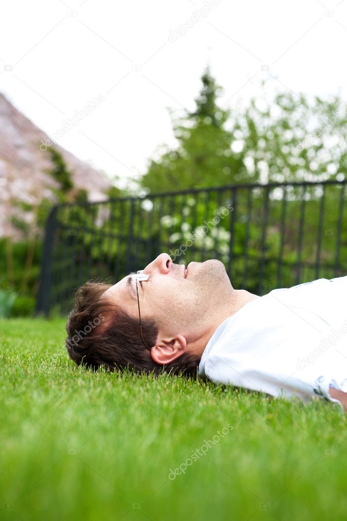 Close-up portrait of young good looking man in white shirt lying on lawn and daydreaming while looking at the sky