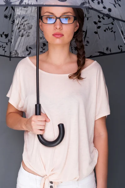 Joven mujer de moda sosteniendo paraguas de pie sobre fondo gris — Foto de Stock