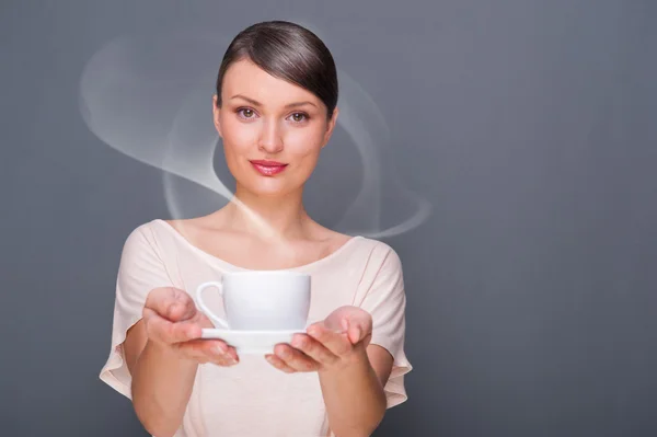 Портрет молодой модной женщины, дающей фотоаппарату горячий кофе или чай на сером фоне — стоковое фото