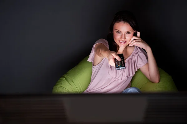 Glad ung kvinna håller fjärrkontrollen och titta på romantisk film av tv — Stockfoto