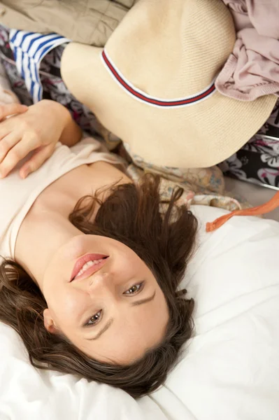 Schöne junge schlanke Frau auf dem Bett drinnen beim Auspacken der Kleidung aus dem Koffer — Stockfoto