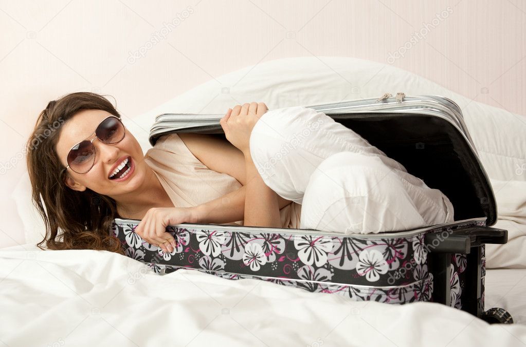 Portrait of young woman preparing for a trip and hiding inside her suitcase