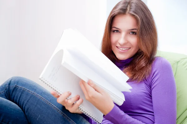 Mujer adulta joven escribiendo en su copybook mientras está sentada en una bolsa de frijoles grande en su casa — Foto de Stock