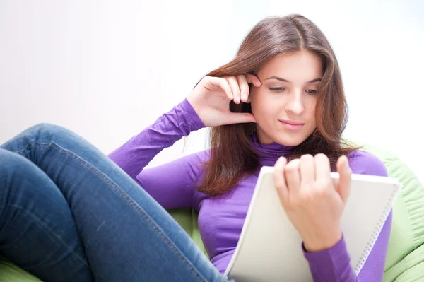 Young adult woman writing in her copybook while sitting on a large beanbag at her home — Stock Photo, Image