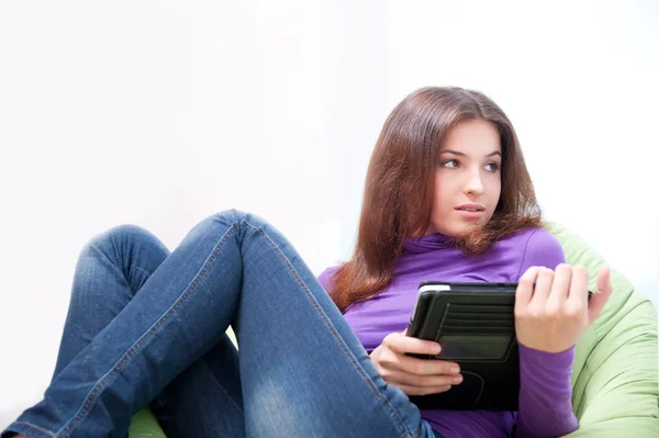 Mujer adulta joven usando su tableta mientras está sentada en una bolsa de frijoles grande en su casa —  Fotos de Stock