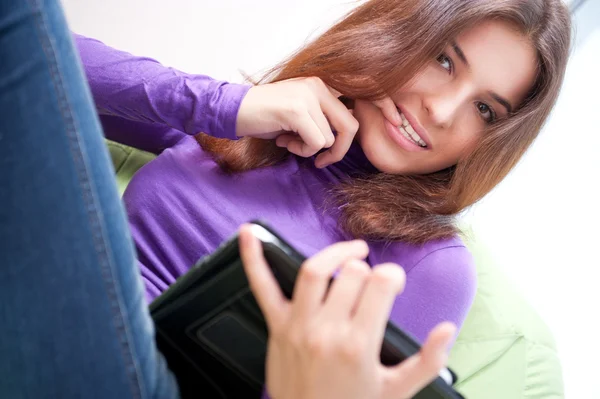 Молодая взрослая женщина за планшетным компьютером, сидя на большой бобовой сумке у себя дома — стоковое фото