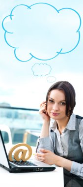 Portrait of a cheerful Business woman sitting on her desk with an at symbol and blank cloud balloon overhead clipart