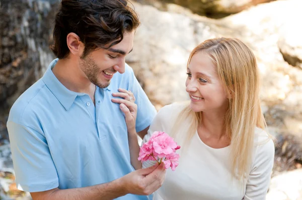 Portrait of love couple embracing outdoor in park looking happy. Man gifting flower to his girl — Stock Photo, Image