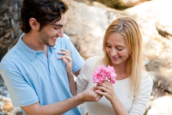Портрет влюбленной пары, обнимающей на открытом воздухе в парке, выглядит счастливой. Мужчина дарит цветок своей девушке — стоковое фото