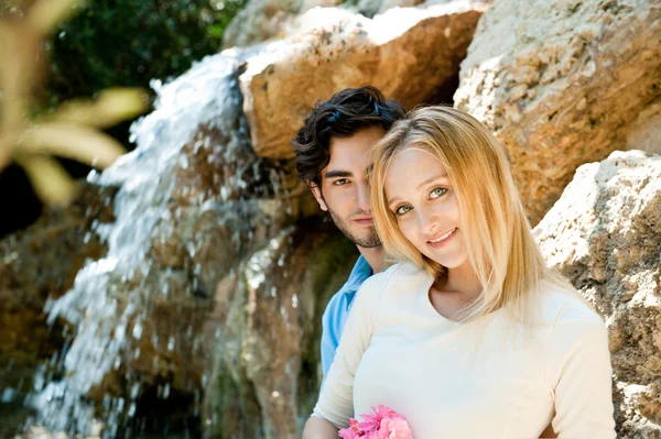 Porträt eines Liebespaares, das sich im Park umarmt und glücklich aussieht. Frau mit Blume. Wasserfall im Hintergrund — Stockfoto
