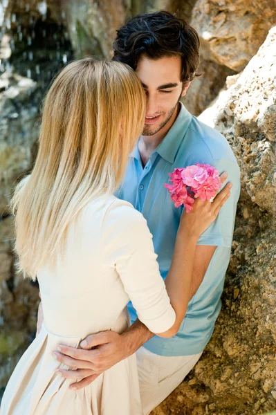 Portret van liefde paar omarmen buiten in park op zoek gelukkig. vrouw bedrijf bloem. waterval op achtergrond — Stockfoto