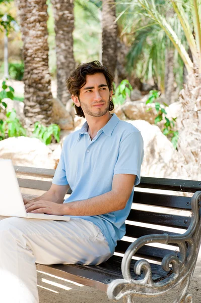 Πορτρέτο ενός νεαρού άνδρα με φορητό υπολογιστή εξωτερική κάθεται σε παγκάκι — Φωτογραφία Αρχείου