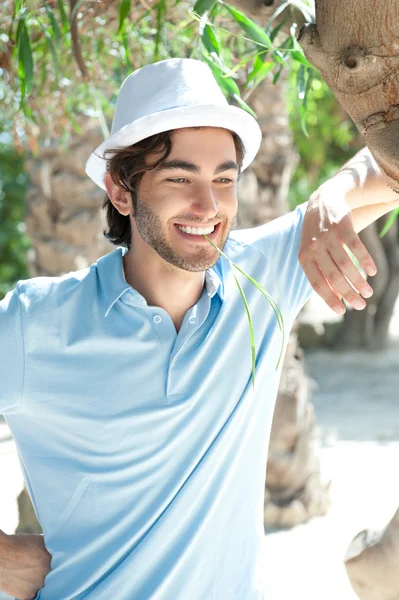 Jeune homme portant un chapeau et des vêtements décontractés dans la journée ensoleillée. Penché sur le palmier au parc d'été — Photo