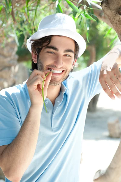 Giovane uomo che indossa cappello e vestiti casual nella giornata di sole. Appoggiato sulla palma al parco estivo — Foto Stock
