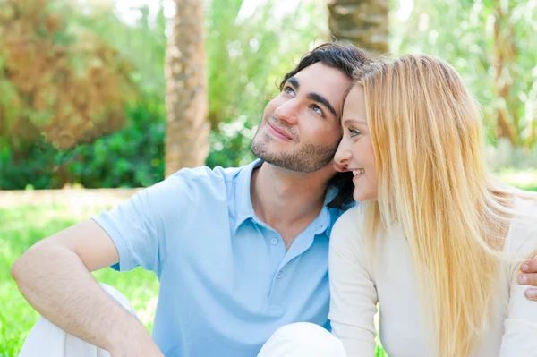 Romantyczna młoda para siedzi razem w parku lata ogarniecie i uśmiechając się — Zdjęcie stockowe