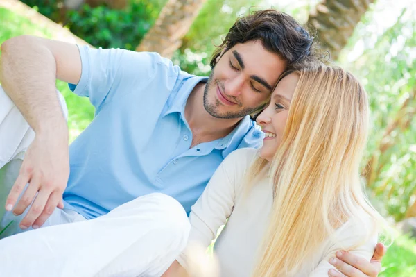 Romántica pareja joven sentados juntos en el parque de verano abrazando y sonriendo —  Fotos de Stock