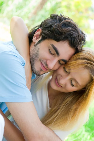 Романтическая молодая пара, сидящая вместе в летнем парке, обнимающая и улыбающаяся — стоковое фото