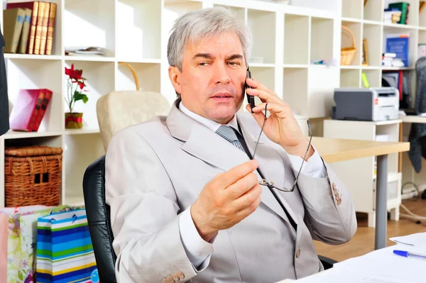 Porträt eines hochrangigen Geschäftsmannes, der im Büro am Telefon sitzt — Stockfoto