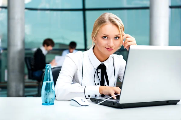 Portrait de belle femme utilisant un ordinateur portable à son lieu de travail sur le fond de l'entreprise — Photo