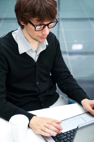 Amical exécutif assis devant un ordinateur portable dans son bureau. Grande fenêtre à l'arrière-plan. Regardant ailleurs, rêvant — Photo