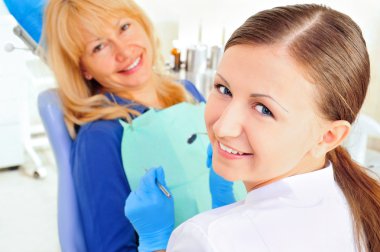 At dentist's office young nurse with adult mature woman, both looking at camera and smiling clipart