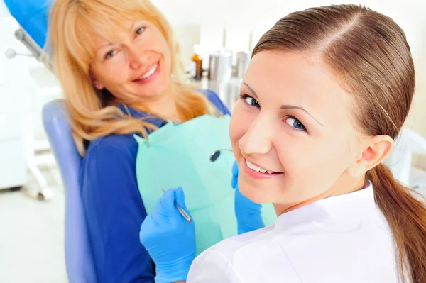 Bij de tandarts Bureau jonge verpleegster met volwassen volwassen vrouw, beide camera kijken en glimlachen — Stockfoto