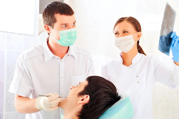 A dentist and a nurse curing young mans teeth — Stock Photo, Image