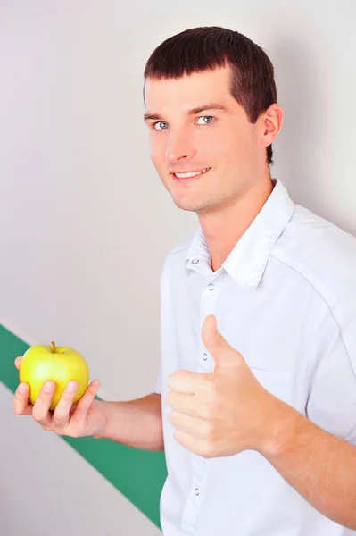 Крупный план счастливого взрослого стоматолога, склоняющегося к стене стоматологической клиники и держащего в руках зеленое яблоко — стоковое фото
