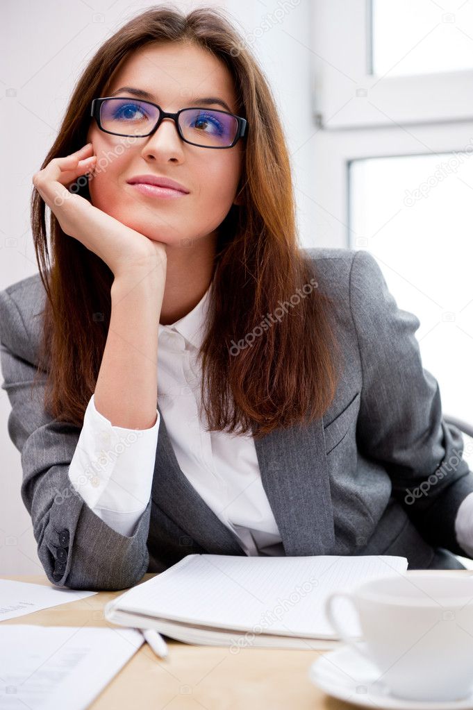 Young businesswoman smiles and daydreaming while working. Vertical shot.
