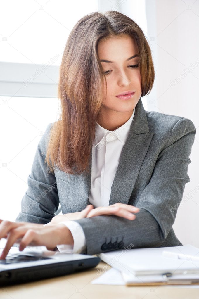 Beautiful business woman looking at papers while working on computer at her office