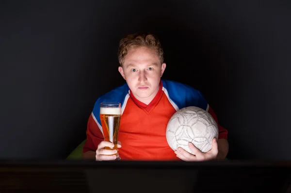 Retrato de jovem assistindo TV tradução do jogo de futebol com sua equipe favorita e segurando bola e bebendo cerveja — Fotografia de Stock