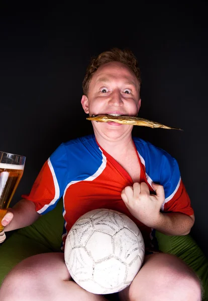 Retrato de jovem assistindo TV tradução do jogo de futebol com sua equipe favorita e beber cerveja e comer peixe salgado — Fotografia de Stock