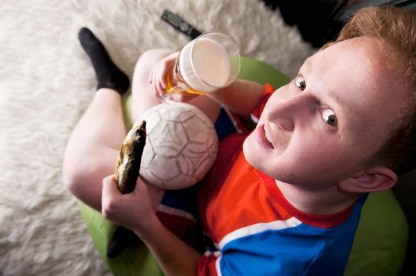 Πορτρέτο του νεαρού βλέποντας τηλεόραση μετάφραση του παιχνιδιού του ποδοσφαίρου με η αγαπημένη του ομάδα και πίνοντας μπύρα και αλμυρό ψάρι. κάτοψη — Φωτογραφία Αρχείου