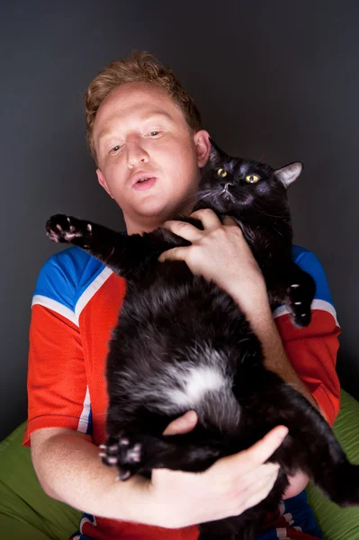Портрет молодого человека, смотрящего телевизионный перевод футбольного матча своей любимой команды со своей кошкой — стоковое фото
