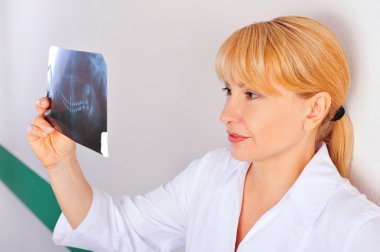 Portrait of smiling caucasian woman doctor wearing uniform standing against wall at hospital looking at xray results of her patient clipart