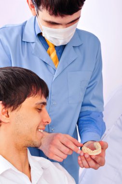 A young male patient in a dentist office looking at plaster cast of his teeth clipart