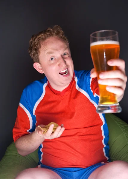 Porträtt av ung man tittar på TV-översättning av fotbollsmatch med hans favoritlag och dricka öl — Stockfoto