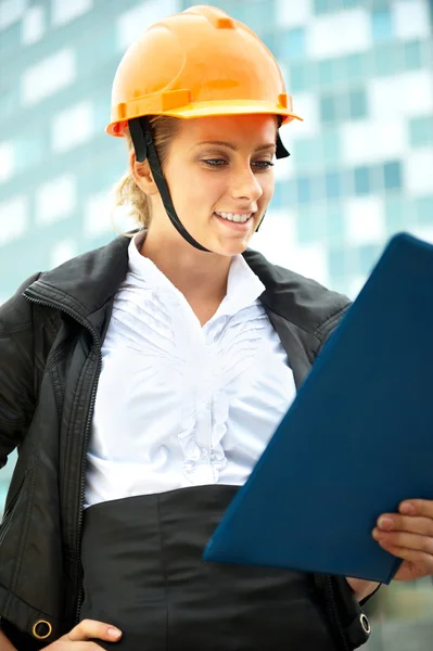 Young architect-woman wearing a protective helmet standing on the building background — Stock Photo, Image