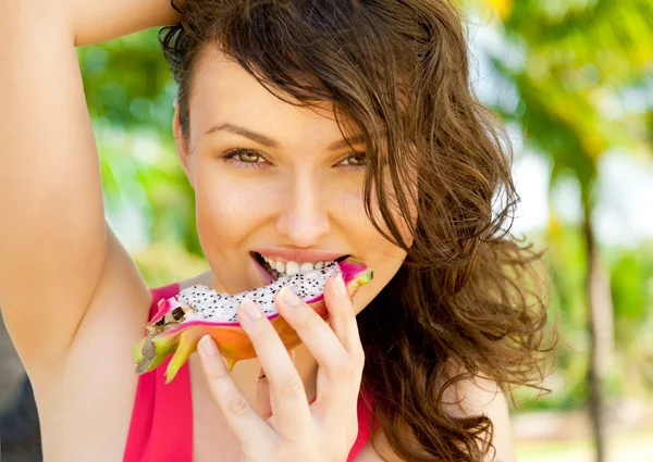 Mujer de vacaciones sonriendo en las vacaciones de verano playa tropical con palmeras. Retrato de modelo femenino bastante feliz comiendo exótica fruta del dragón asiático . — Foto de Stock