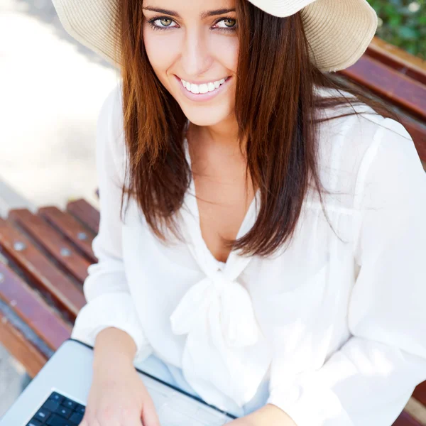 Mujer joven elegante con sombrero de paja y vestido blanco con lapto —  Fotos de Stock