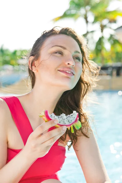 Frau sitzt in einem Schwimmbad und isst Drachenfrucht — Stockfoto