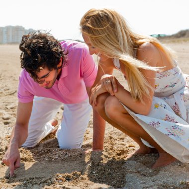 Couple in love drawing a heart in the sand while relaxing at bea clipart