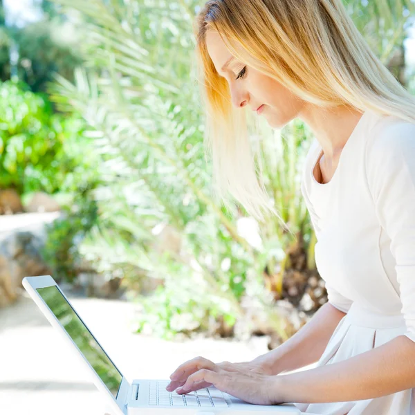 Mulher bonita usando laptop enquanto sentado relaxado no banco em s — Fotografia de Stock