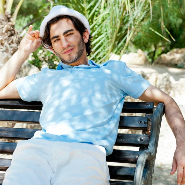 Portrait d'un beau jeune homme assis au soleil sur un banc à — Photo