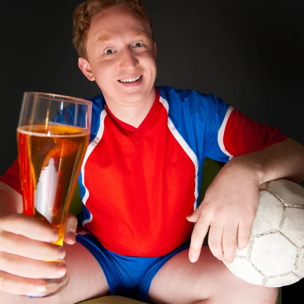 Jovem segurando bola de futebol e cerveja e assistindo TV Translati — Fotografia de Stock